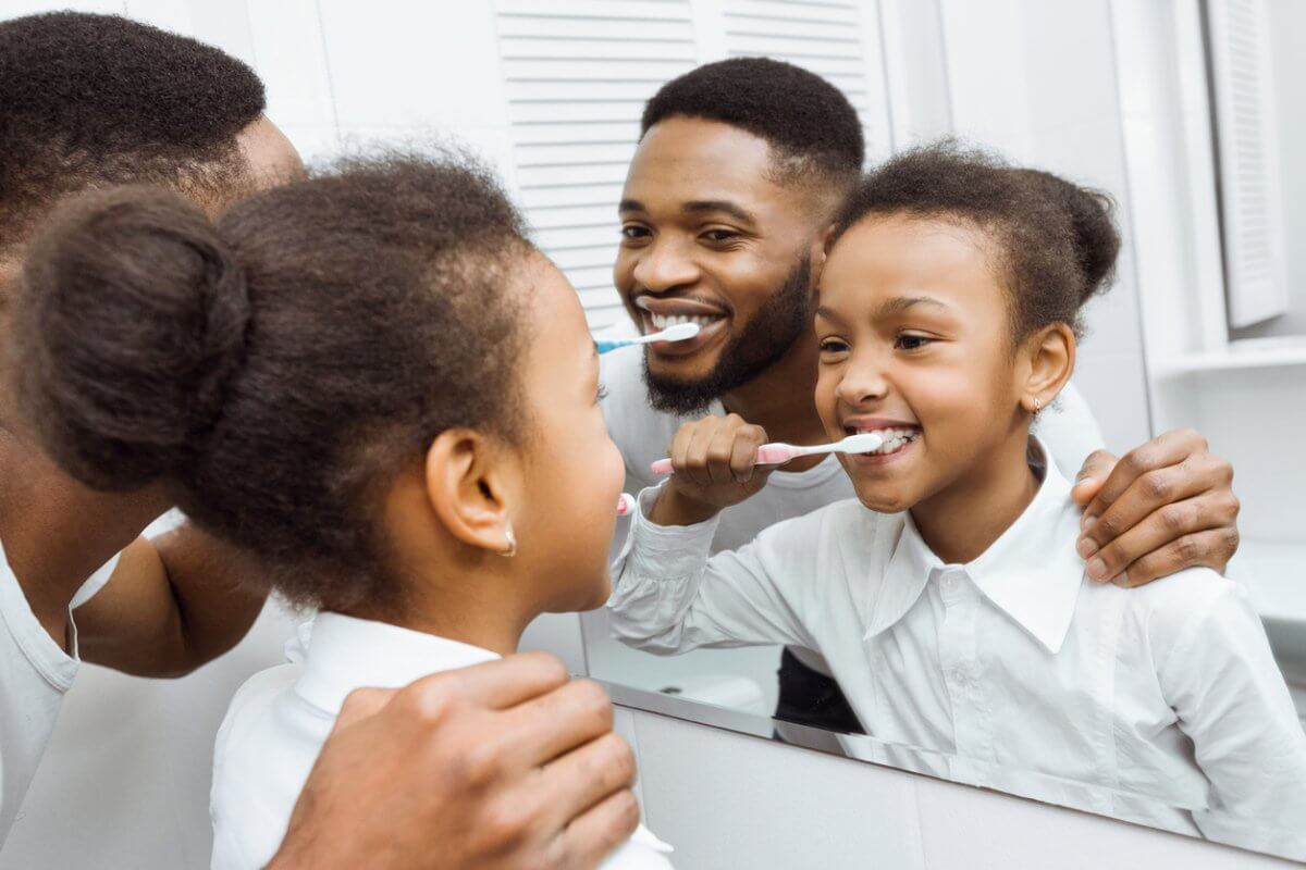 Father And Daughter Brushing Teeth Together Looking In Bathroom Mirror