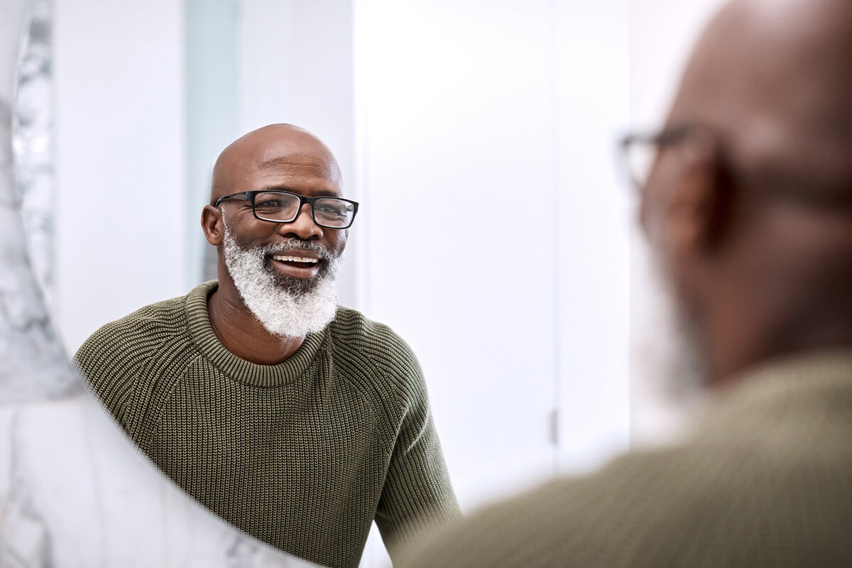 older man with beard looking in a mirror and smiling