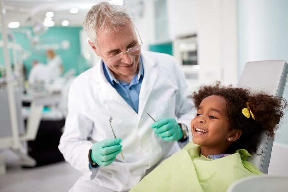 young girl smiling in dental exam chair with dentist beside her