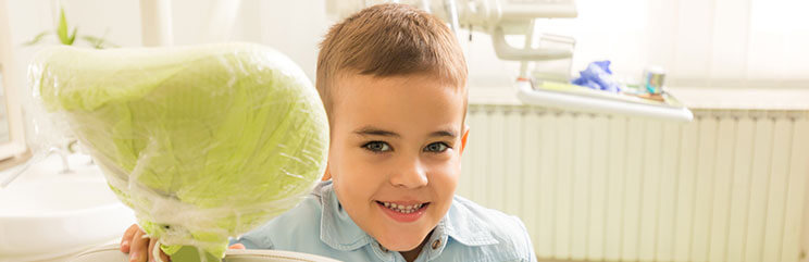 A young boy standing next to a dental exam chair smiling