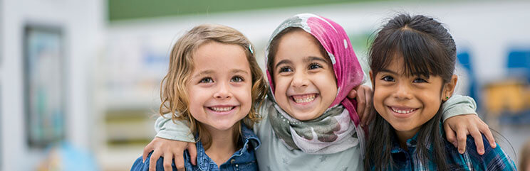 Three young girls smiling wide with their arms around each other