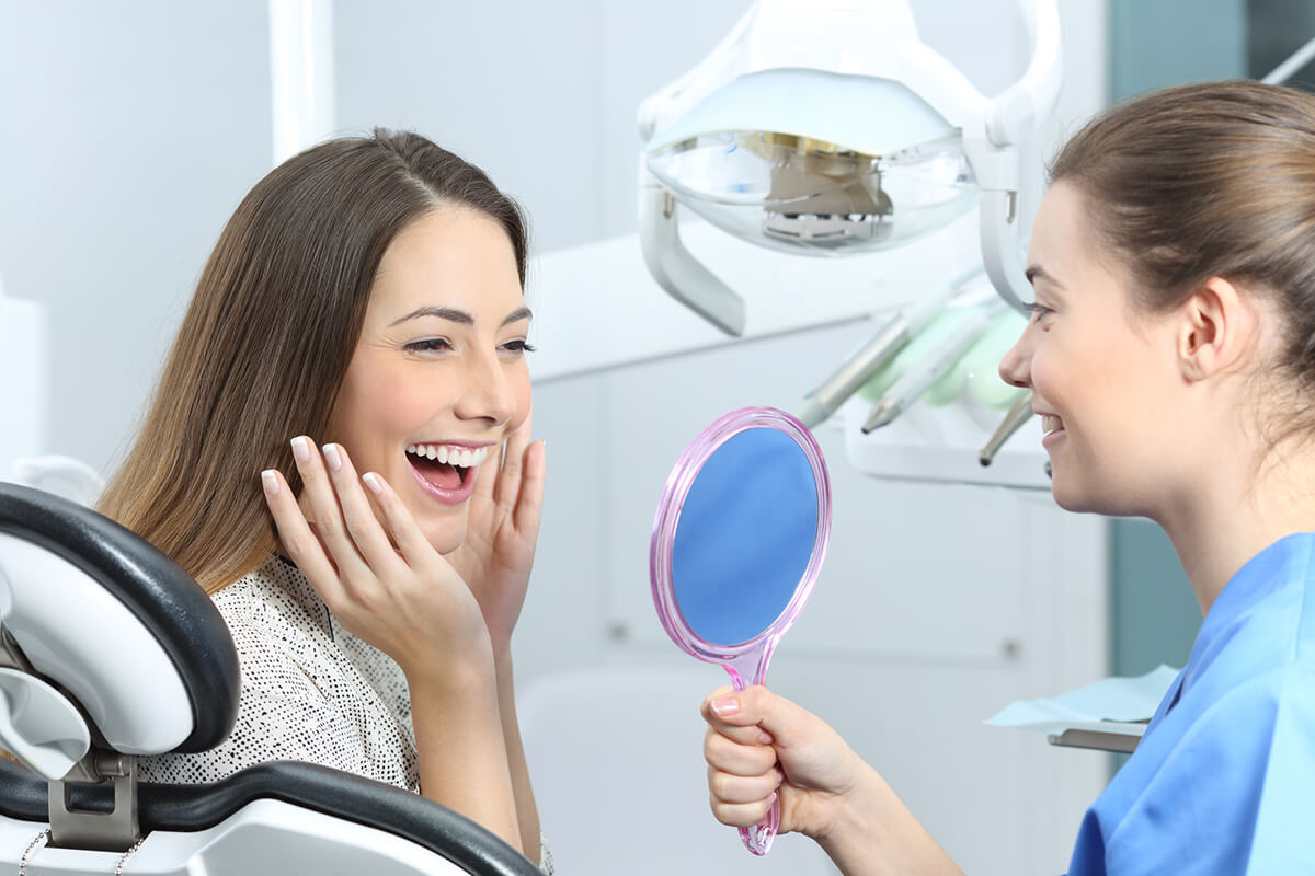 dental assistant holding up a hand mirror for a female patient