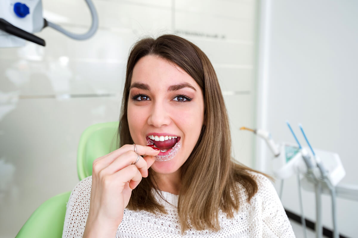 young woman in dental chair putting dental aligner in her mouth